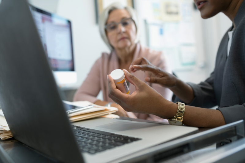 A CVS Pharmacy representative at a computer discussing a vial of medication with an elderly woman