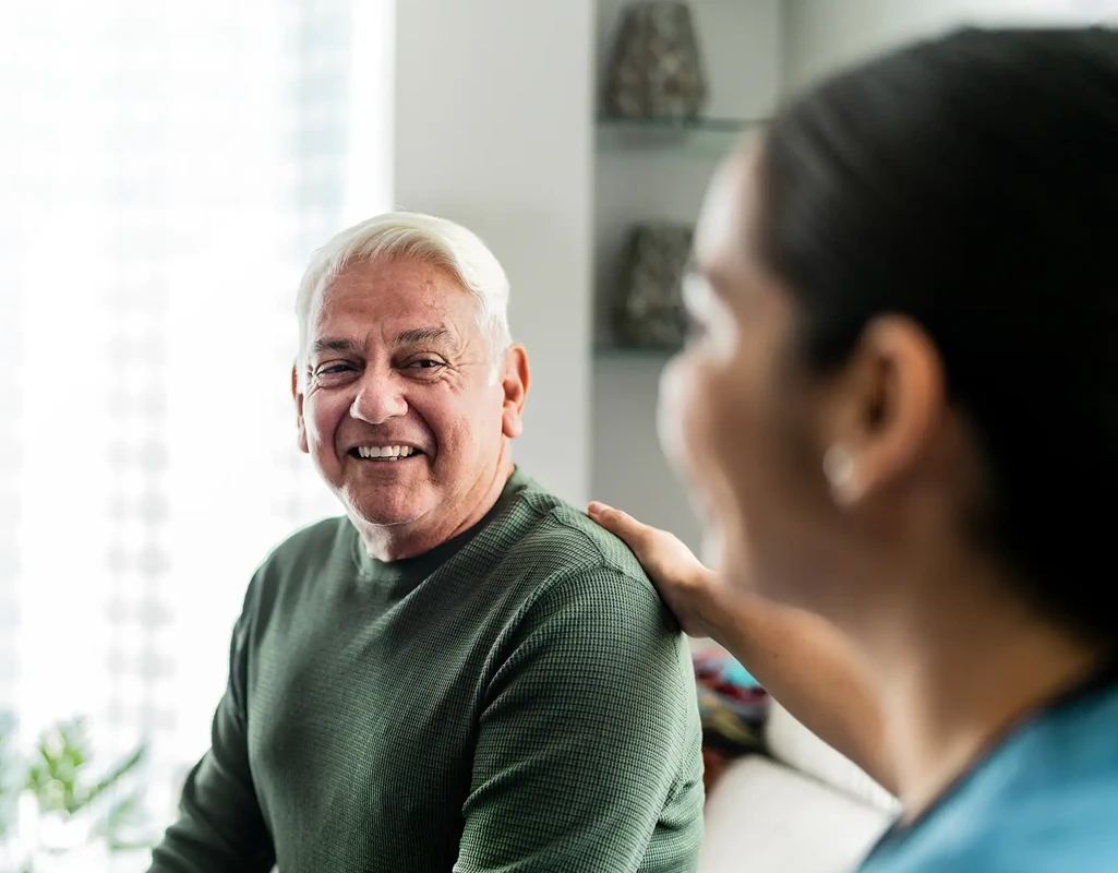An older man is seated having a conversation with a female nurse